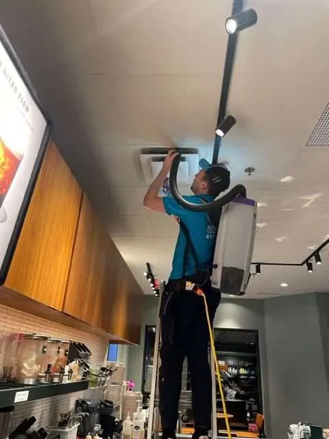 A person is on a ladder, installing or repairing ceiling lights in a commercial setting.